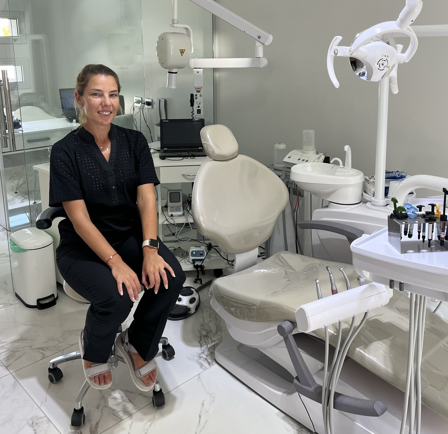 foto de odontóloga Débora Márquez, sentada en su puesto 
                de trabajo, mirando a la cámara junto a su sillón y 
                todo su equipamiento